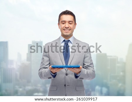 business, people and technology concept - happy smiling businessman in suit holding tablet pc computer over city background