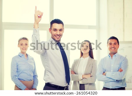 business and office concept - smiling handsome businessman with team in office and finger up