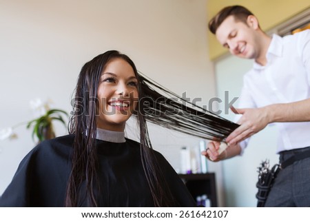 beauty, hairstyle and people concept - happy young woman and hairdresser cutting hair tips at salon