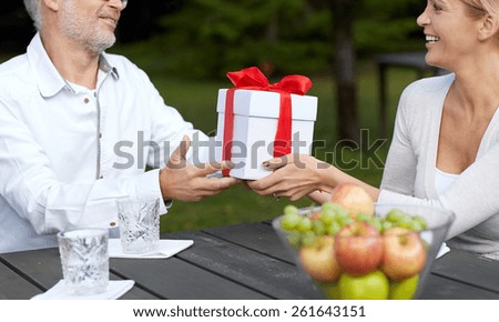 family, generation, home, holidays and people concept - happy woman giving birthday present to senior man or father at dinner in summer garden