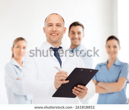 medicine, profession, teamwork and healthcare concept - smiling male doctor with clipboard writing prescription over group of medics
