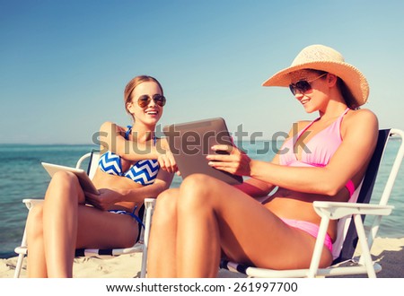 summer vacation, travel, technology and people concept - smiling women with tablet pc computers sunbathing in lounge on beach