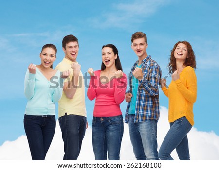 friendship, dream, teamwork, gesture and people concept - group of smiling teenagers showing triumph gesture over blue sky with white cloud background