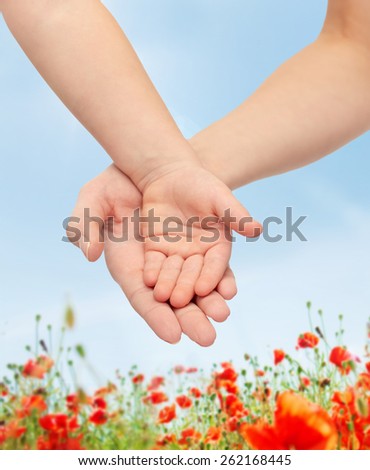 people, charity, family, children and advertisement concept - close up of woman and little child hands holding empty palms over blue sky and poppy field background