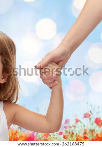 people, charity, family and adoption concept - close up of woman and little girl holding hands over blue lights and poppie field background