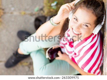 summer holidays and technology concept - teenage girl with headphones listening to music outside