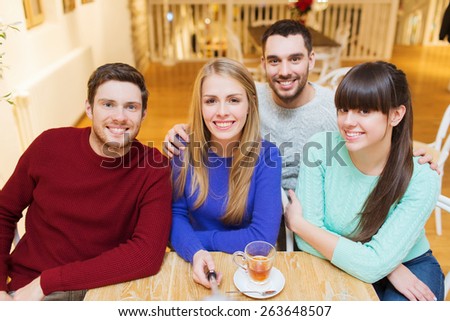 people, leisure, friendship and technology concept - group of happy friends with selfie stick taking picture and drinking tea at cafe