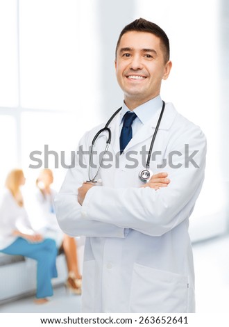 healthcare, profession, people and medicine concept - smiling male doctor in white coat over group of medics at hospital background