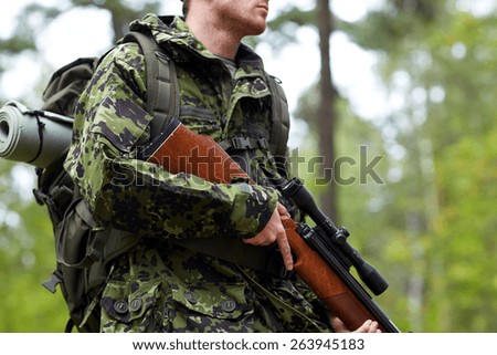 hunting, war, army and people concept - close up of young soldier, ranger or hunter hands holding gun and walking in forest