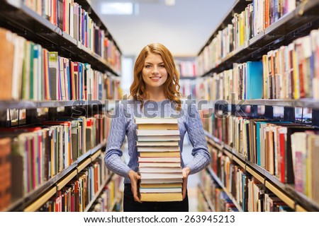 people, knowledge, education and school concept - happy student girl or young woman with stack of books in library