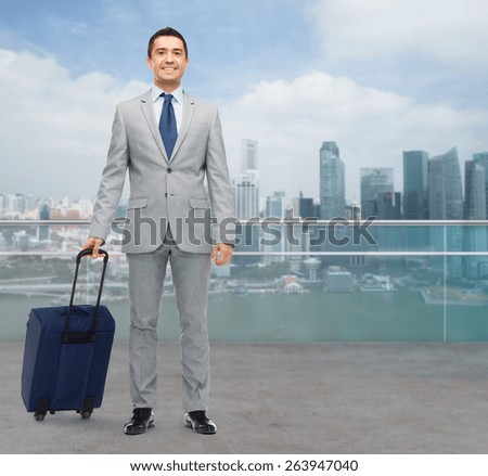 business trip, traveling, luggage and people concept - happy businessman in suit with travel bag over city background