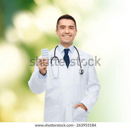healthcare, profession, people and medicine concept - smiling male doctor in white coat with tablets over green background