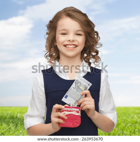 finances, childhood, people and savings concept - happy little girl with purse and paper euro money over blue sky and grass background