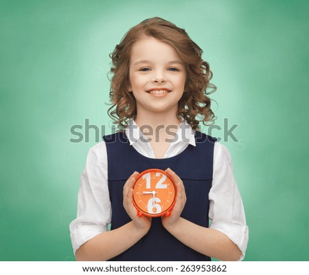 people, childhood, time and punctuality concept - happy girl with alarm clock over green chalk board background