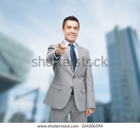 business, people and office concept - happy smiling businessman in suit pointing at you over city background