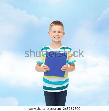 education, childhood and school concept - smiling little student boy with blue book over blue cloudy sky background