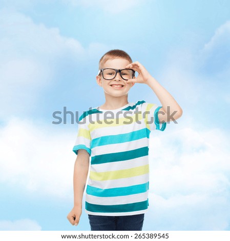 vision, education, childhood and school concept - smiling little boy in eyeglasses over blue sky with white clouds background
