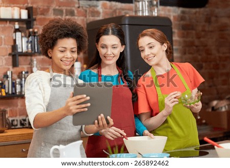 cooking class, friendship, food, technology and people concept - happy women with tablet pc computer in kitchen