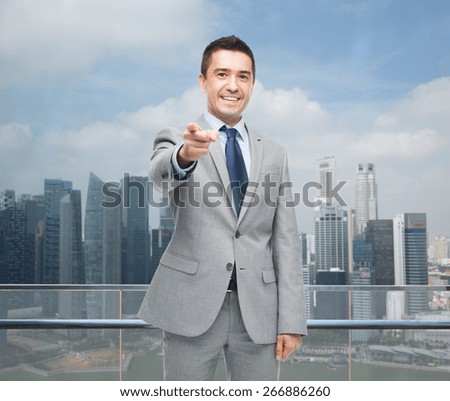 business, people and office concept - happy smiling businessman in suit pointing at you over city background