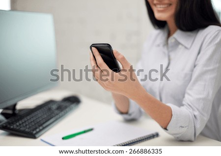 business, education, technology and people concept - close up of happy woman with notebook and computer texting on smartphone at office