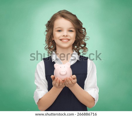 people, money, finances and savings concept - happy girl holding piggy bank on palms over green chalk board background