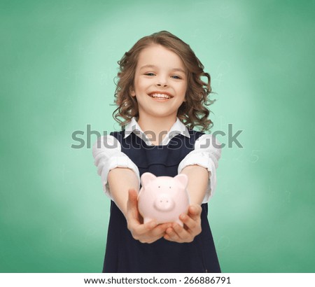 people, money, finances and savings concept - happy girl holding piggy bank on palms over green chalk board background
