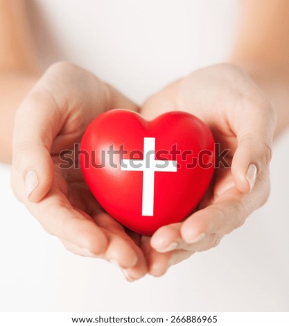 religion, christianity and charity concept - female hands holding red heart with christian cross symbol
