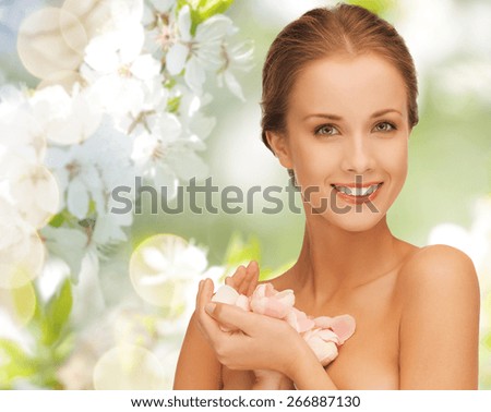 summer, spring, beauty, people and health concept - beautiful young woman holding flower petals over green blooming garden background