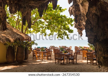 leisure, travel and tourism concept - view to open-air restaurant on beach resort from cave