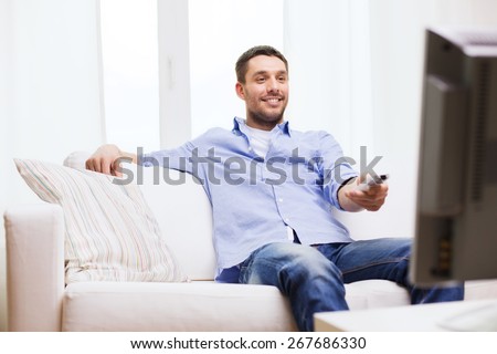 home, technology, people and entertainment concept - smiling man with tv remote control at home