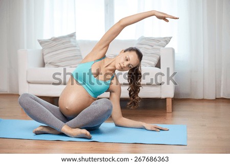 pregnancy, sport, yoga, people and healthy lifestyle concept - happy pregnant woman exercising and stretching on mat at home
