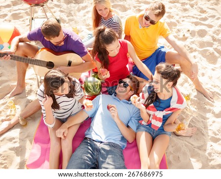 summer holidays, vacation, music, happy people concept - group of happy friends having picnic and playing guitar on beach