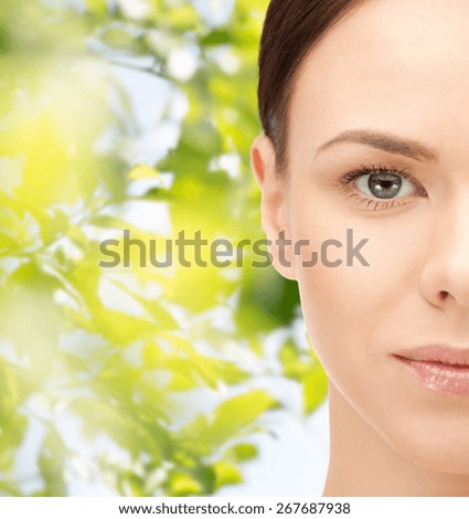 beauty, people, ecology, organic and health concept - beautiful young woman face over green leaves background