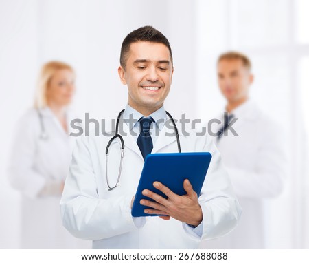 healthcare, profession, people and medicine concept - smiling male doctor in white coat with tablet pc over group of medics at hospital background