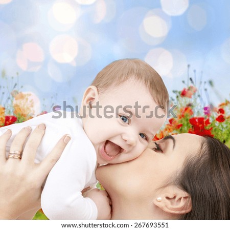 people, family, motherhood and children concept - happy mother hugging adorable baby over blue lights and poppy field background
