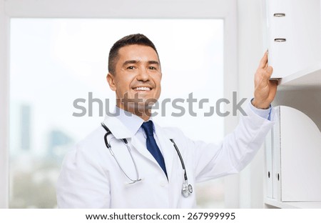 medicine, profession, technology and people concept - happy male doctor taking folder from shelf in medical office