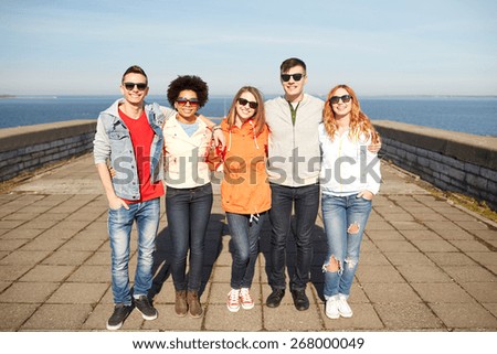tourism, travel, people and leisure concept - group of happy teenage friends in sunglasses hugging on city street