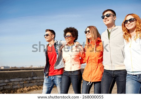 tourism, travel, people and leisure concept - group of happy teenage friends walking along city street