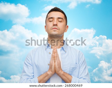 faith in god, religion and people concept - happy man with closed eyes praying over blue sky with clouds background