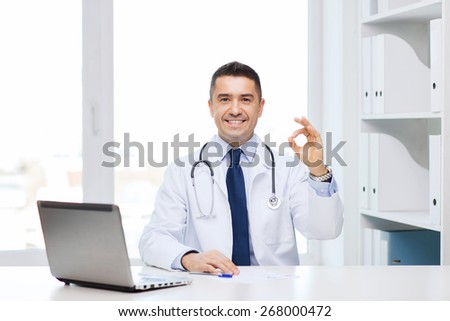 profession, gesture, people, technology and medicine concept - smiling male doctor in white coat with laptop pomputer showing ok in medical office