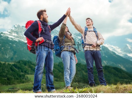 travel, tourism, hike, gesture and people concept - group of smiling friends with backpacks making high five over alpine mountains background