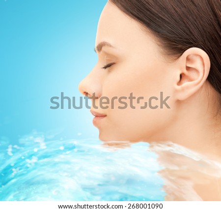 beauty, people, freshness, purity and health concept - face of beautiful young woman and water splash over blue background
