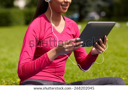 fitness, technology, people and sport concept - close up of smiling african american woman with tablet pc computer sitting on mat outdoors