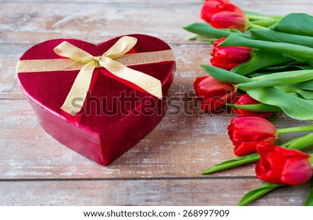 flowers, valentines day and holidays concept - close up of red tulips and heart shaped chocolate box on wooden table