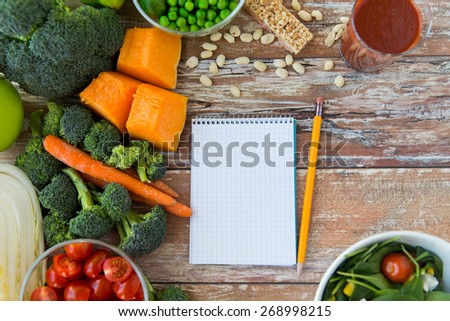 healthy eating, vegetarian food, advertisement and culinary concept - close up of ripe vegetables and notebook with pencil on wooden table
