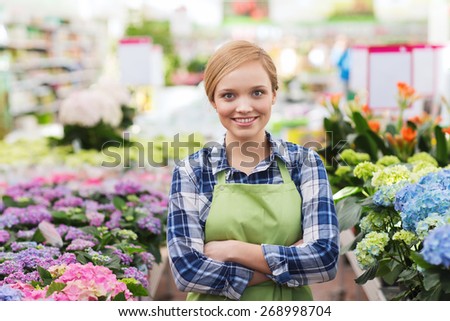 people, gardening and profession concept - happy woman with flowers in greenhouse