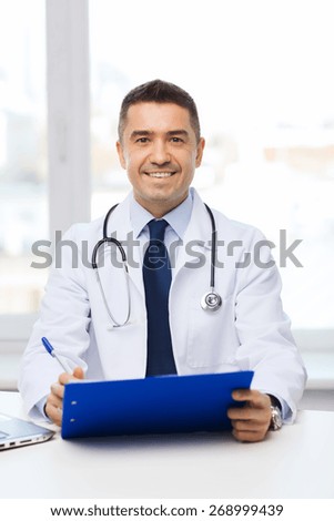 medicine, profession, technology and people concept - happy male doctor with clipboard in medical office