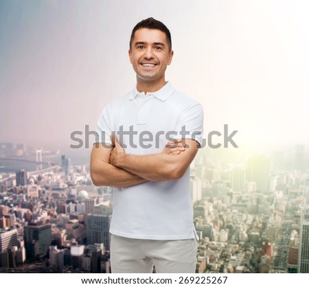 happiness and people concept - smiling man in white t-shirt with crossed arms over city background