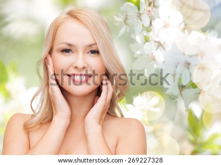 beauty, people, summer, spring and health concept - beautiful young woman touching her face over green blooming garden background