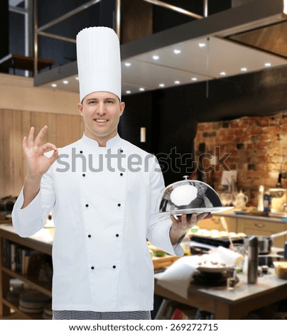 cooking, profession, gesture and people concept - happy male chef cook holding cloche and showing ok sign over restaurant kitchen